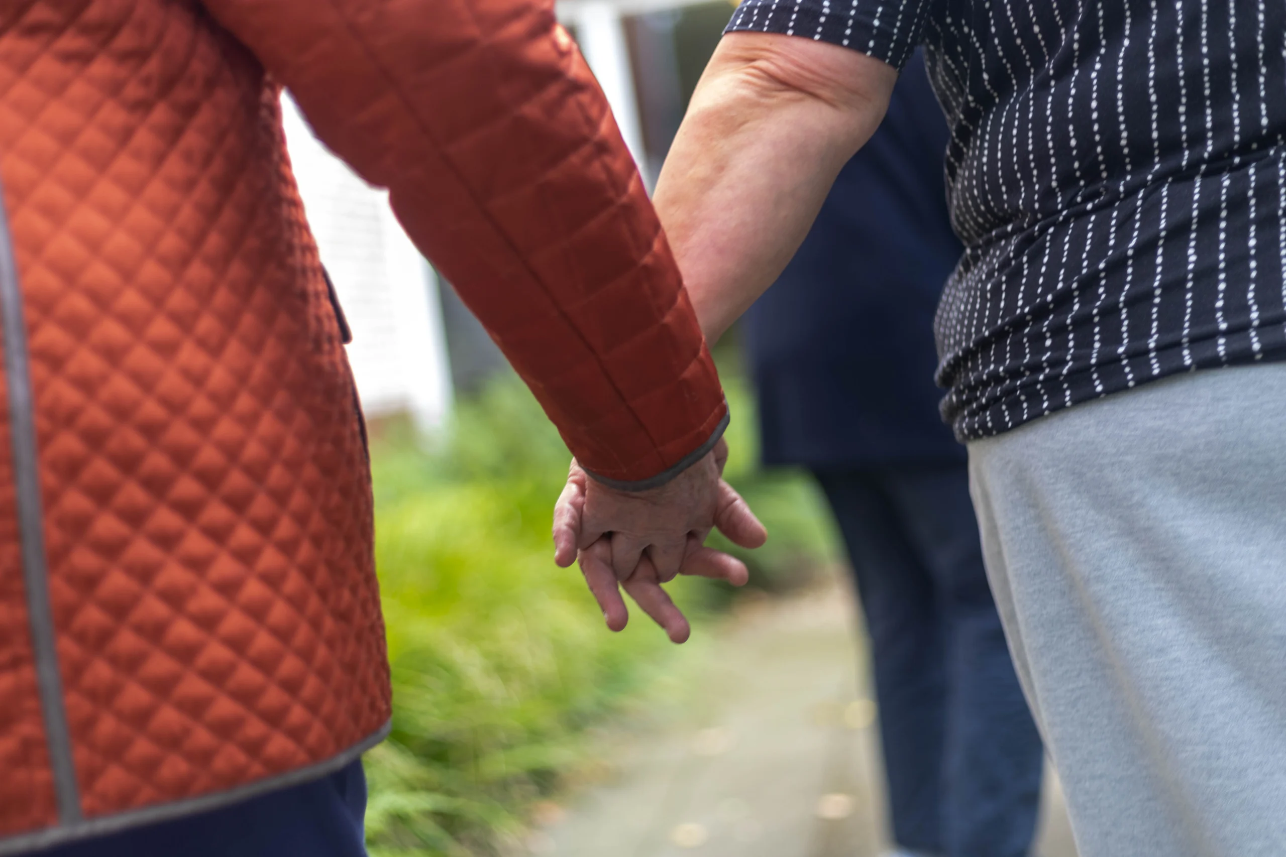 Twee handen die elkaar vasthouden met groene grasachtige achtergrond en twee personen zichtbaar