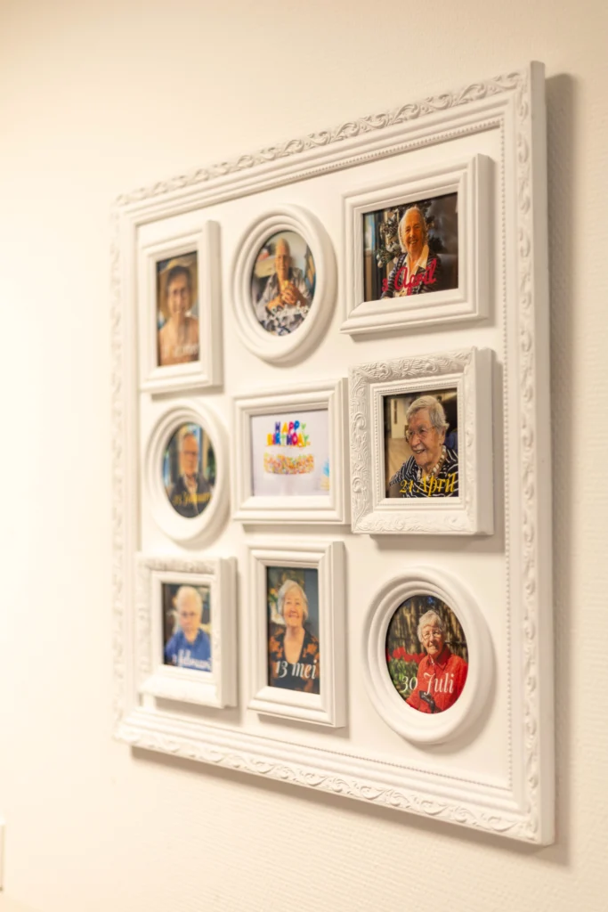 Witte lijst met negen ingelijste foto's van mensen en een kleurrijke happy birthday taart in het midden