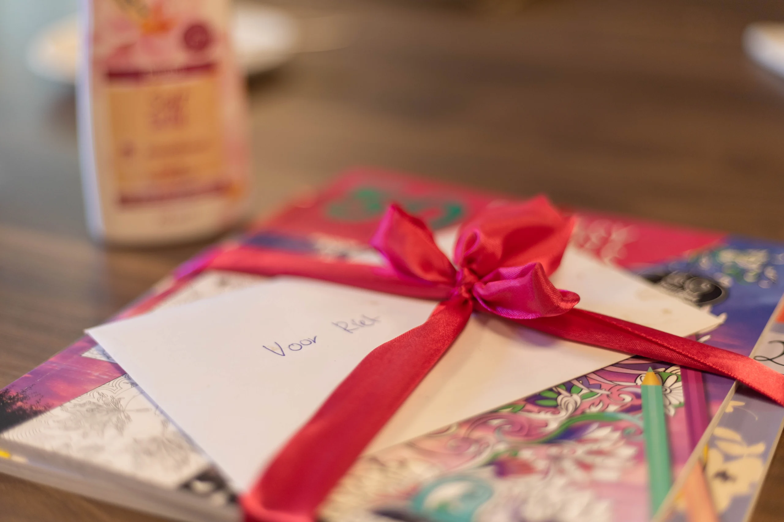 Gestapeld pakket met kaart en felroze strik op houten tafel, kleurplaten, potloden en verzorgingsproduct zichtbaar