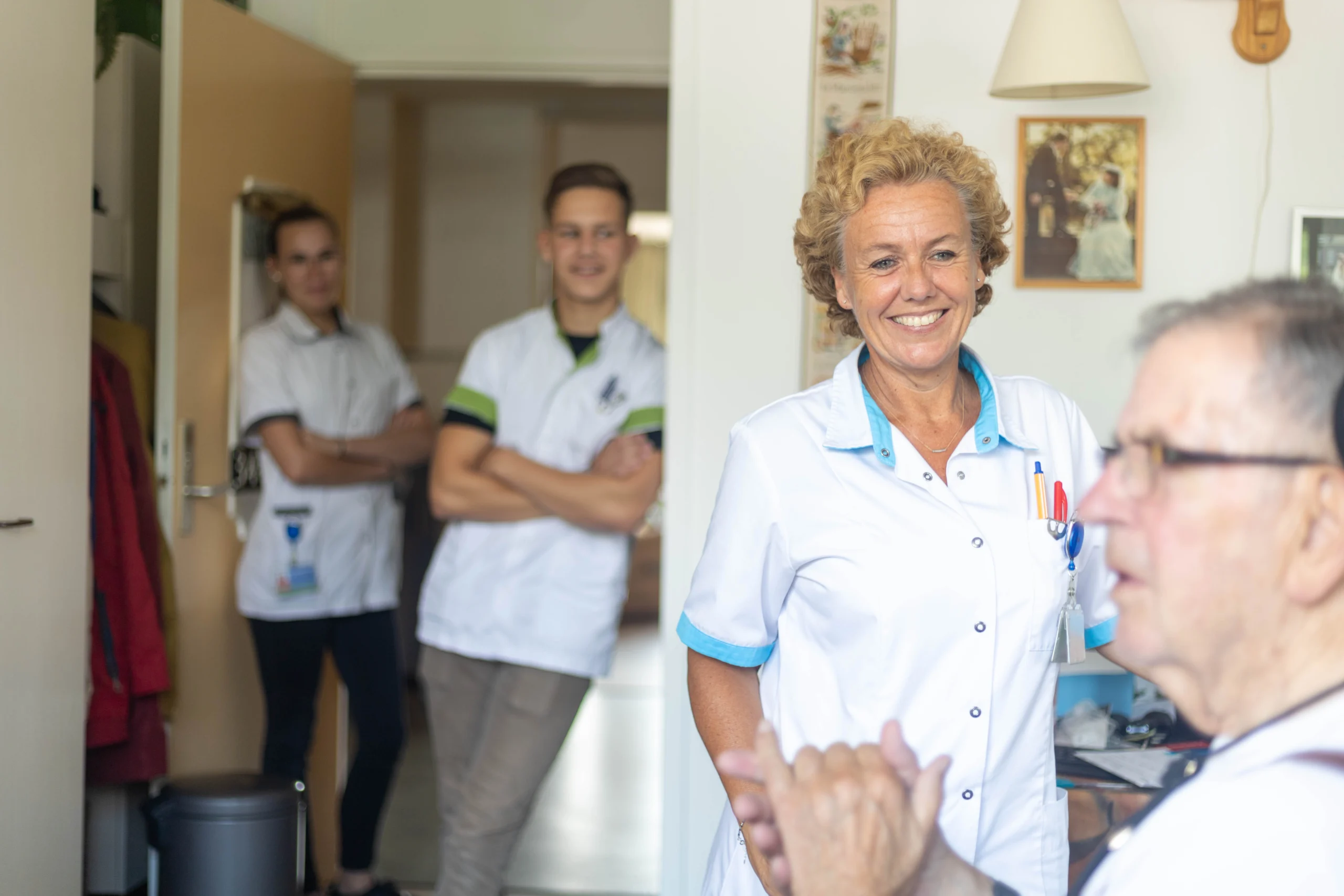 Groep mensen in zorgomgeving met glimlachende oudere man en verzorgers in witte uniformen