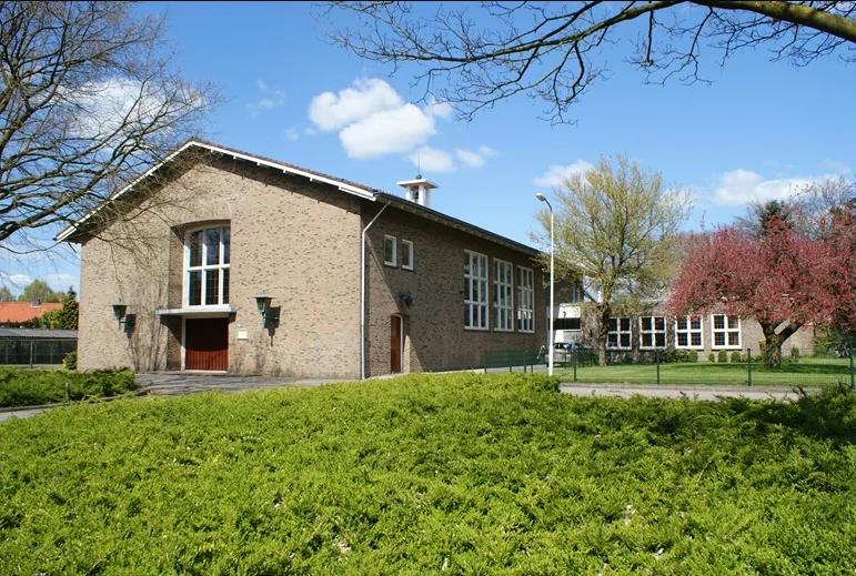 Modern bakstenen gebouw met grote ramen en groen perk voorzijde, heldere blauwe lucht en bomen